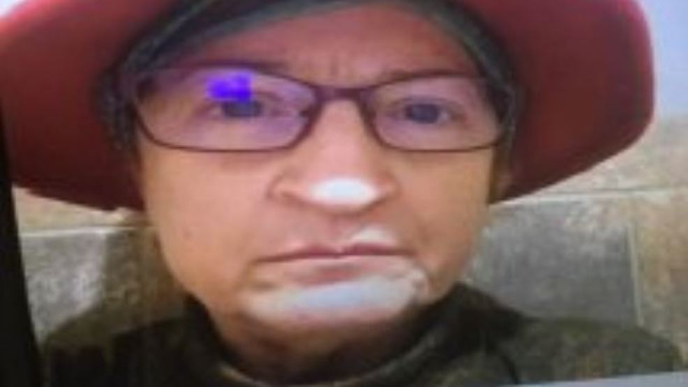 The missing woman looks into the camera, wearing a red hat and glasses.
