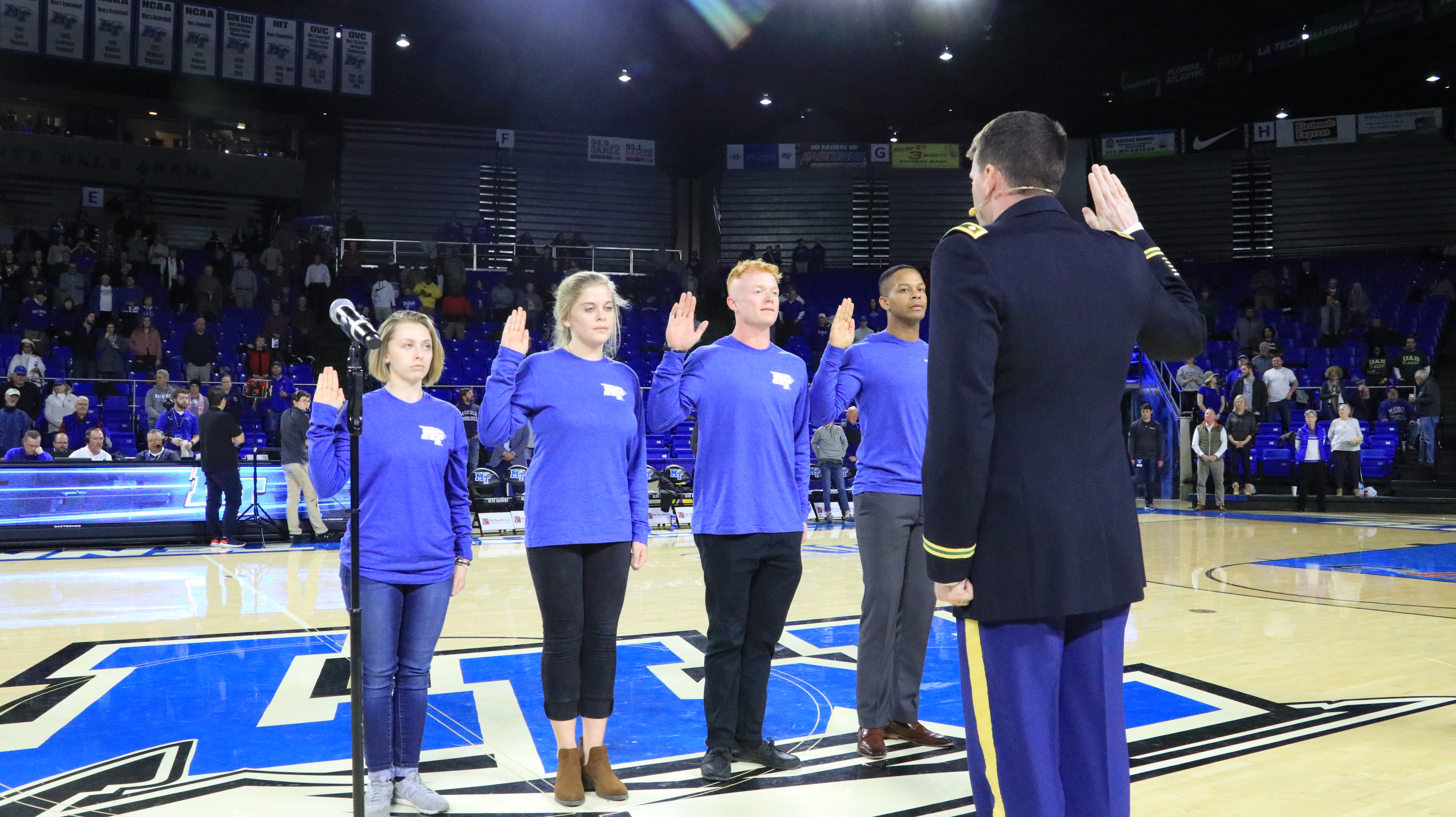 Four MTSU students raise their hands during the Oath of Enlistment ceremony while standing on the floor of the basketball court in Murphy Center.