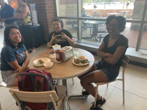 Three young women gather at a table in the Farmers Market to enjoy the fresh food.