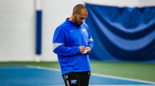 MTSU Men's Tennis coach Jim Boredame stands on a tennis court while writing a note.