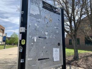 A near empty message board sits on a quiet campus sidewalk.