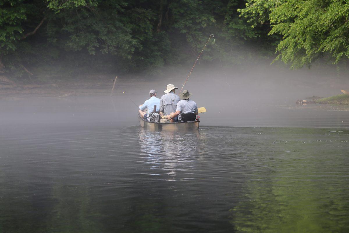 A canoe with three fishermen slips downriver into the fog of a Saturday morning. (Photo by Ethan Pickering)