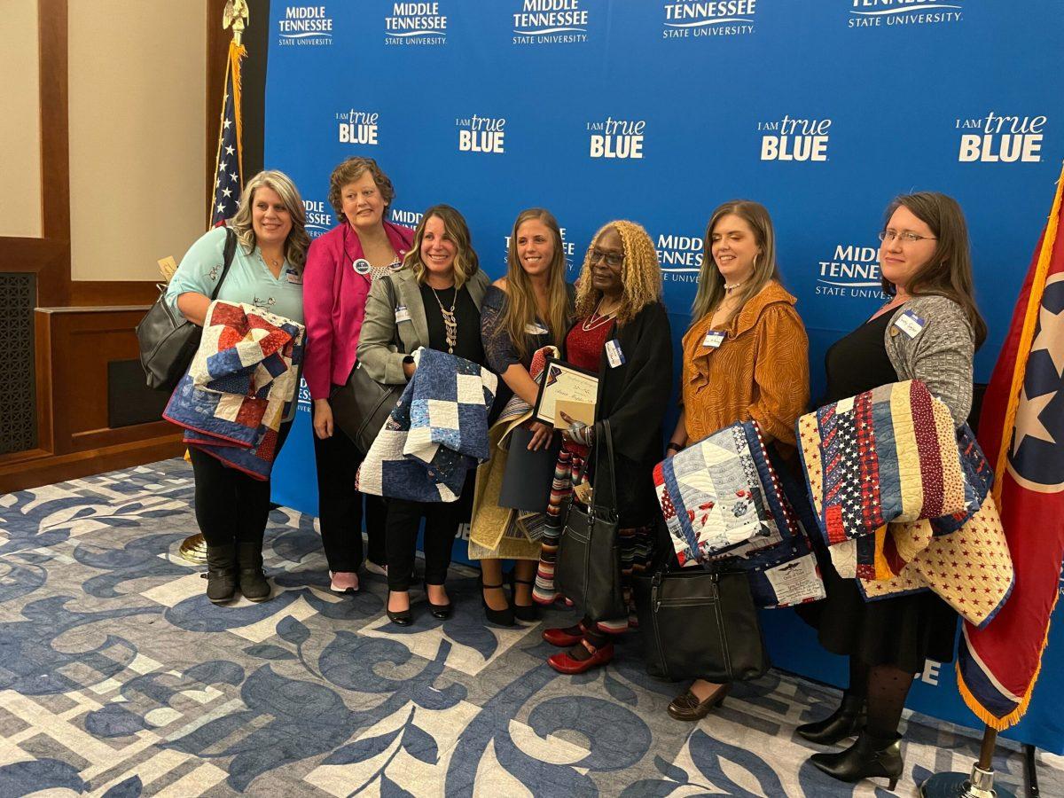 Left to right — Kelly Barnes, Anna Maria Butler, Patricia Cooper, Karlie Franks, Anna Mapps-Stanley, Erica McMurray, and Christy Sigler hold their patriotic quilts at MTSU's Women Warriors event. (Photo by Lillian Chapman)