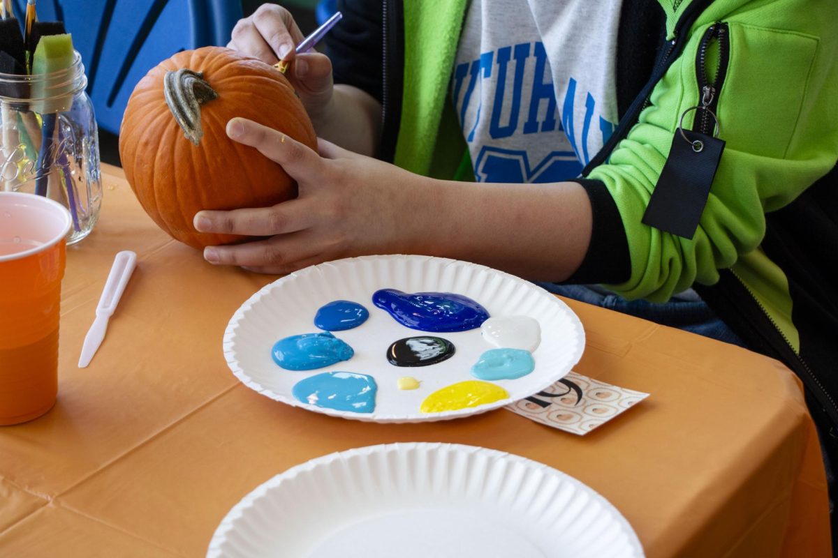 A student meticulously paints a multicolor design onto their pumpkin at the College of Education's pumpkin painting event on Oct. 22, 2025, in the COE foyer.