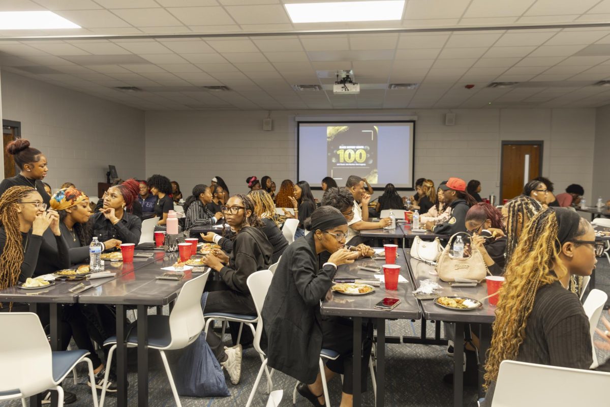 A full room of attendees eats and chats as a Black History flyer is displayed during the Seat at the Table event on Feb. 10, 2026. 