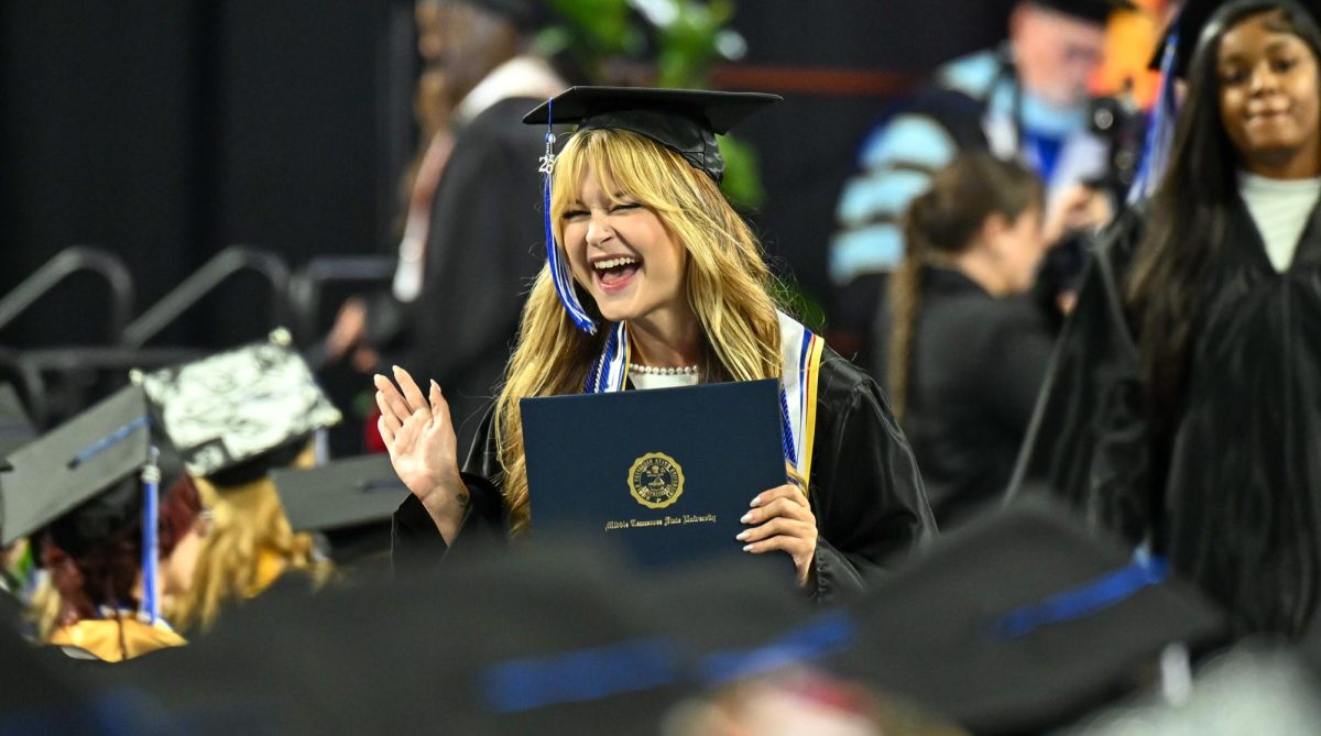 MTSU graduate Olivia Kilpatrick waves to a fellow graduate while walking down the center alley during spring commencement inside the Murphy Center on May 9, 2026.