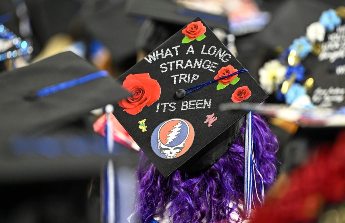 A graduate sits  with a mortarboard decorated with the phrase "what a long strange trip its been" referencing the 1977 Grateful Dead album during spring commencement inside the Murphy Center on May 9, 2026.
