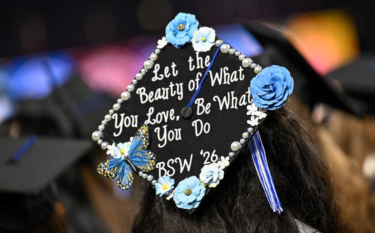 A graduate stands during the national anthem with a mortarboard decorated with the phrase "let the beauty of what you love, be what you do" during spring commencement inside the Murphy Center on May 9, 2026.