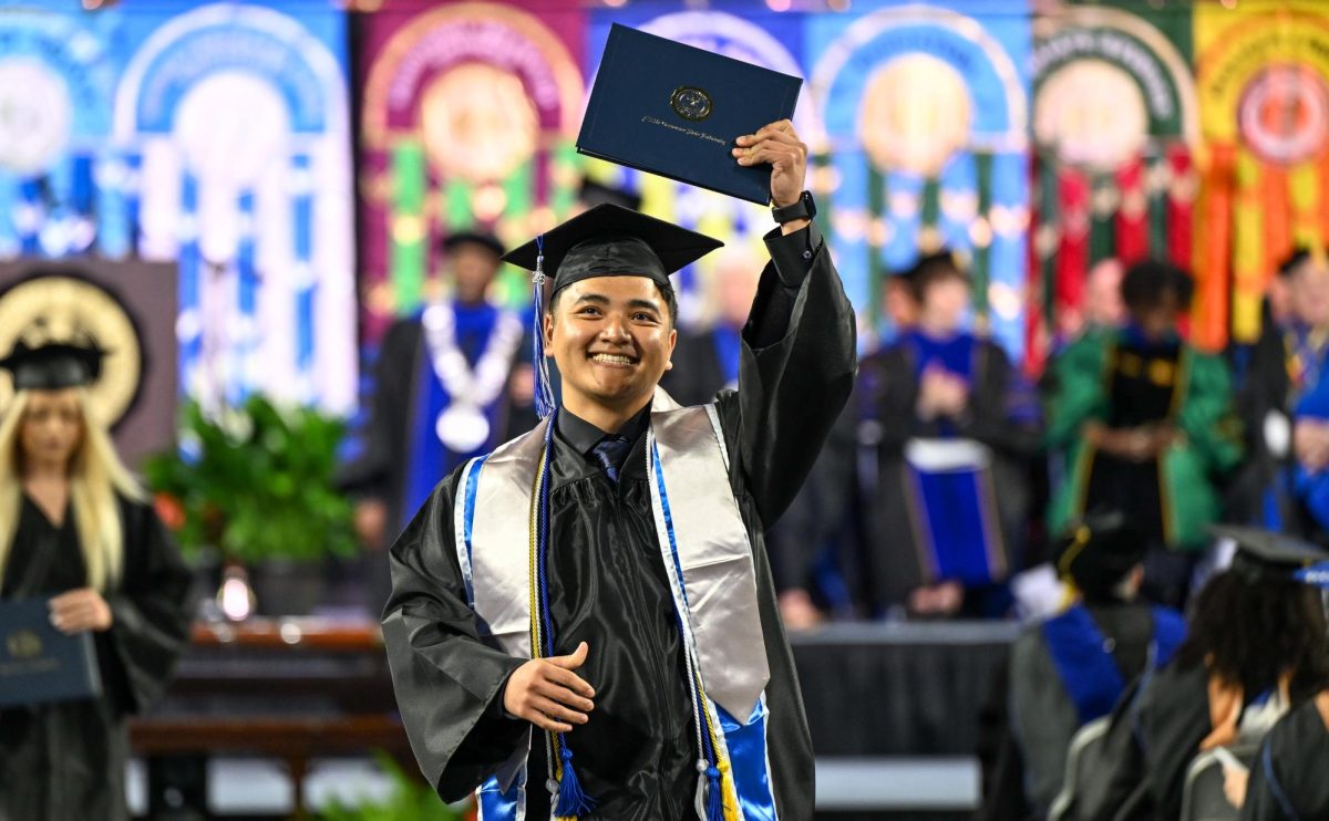 MTSU graduate Thang Lian holds up his diploma in celebration during spring commencement inside the Murphy Center on May 9, 2026.