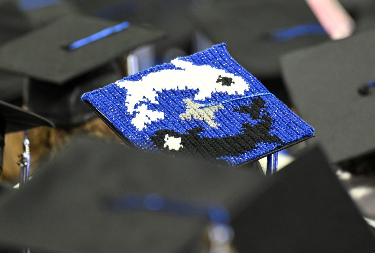 A graduate sits among the sea of black motorboards with a mortarboard decorated with two koi fish during spring commencement inside the Murphy Center on May 9, 2026.
